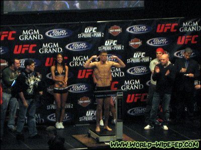 Nate Diaz flexes at 156 as announcer Joe Rogan, brother Nick Diaz, ring girls Logan Stanton and Arianny Celeste, his opponent's brother Jason Guida, UFC President Dana White, and ring announcer Bruce Buffer look on.